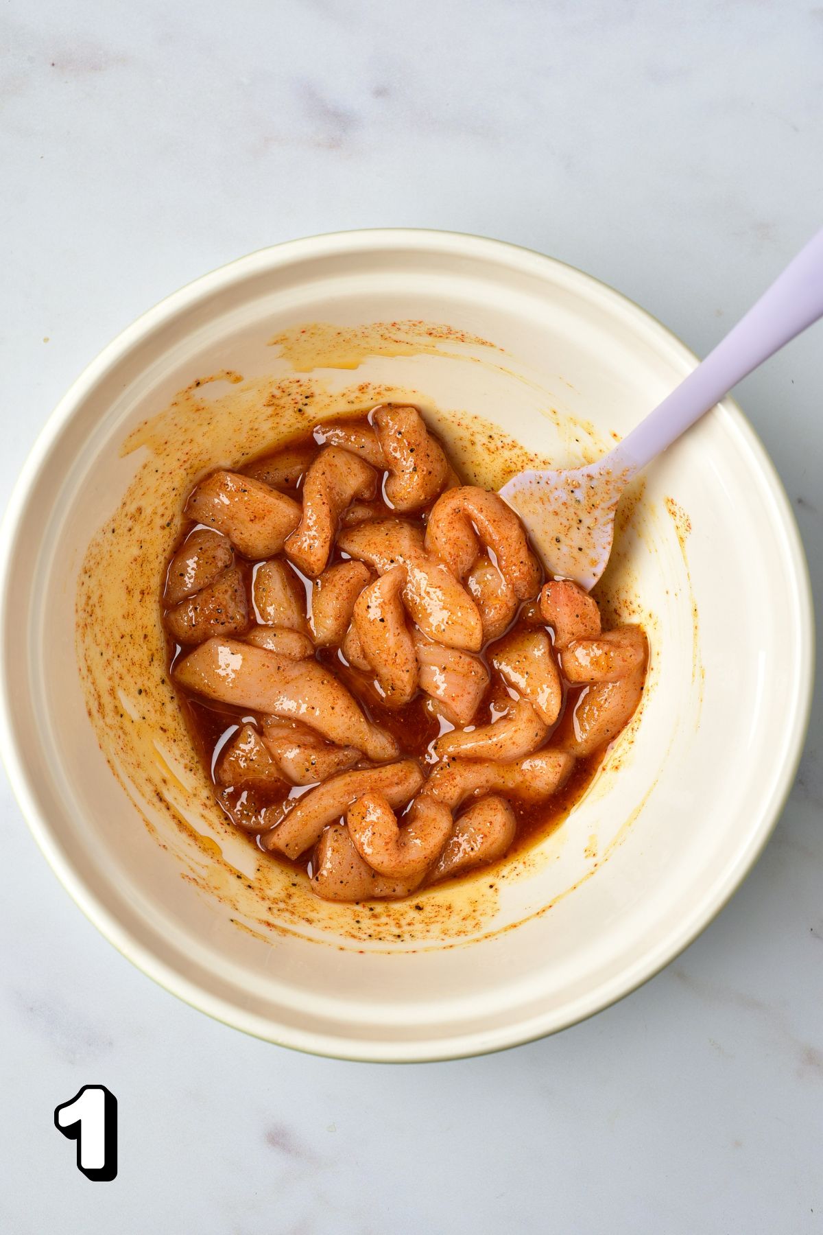 Raw chicken strips in a bowl of marinade.