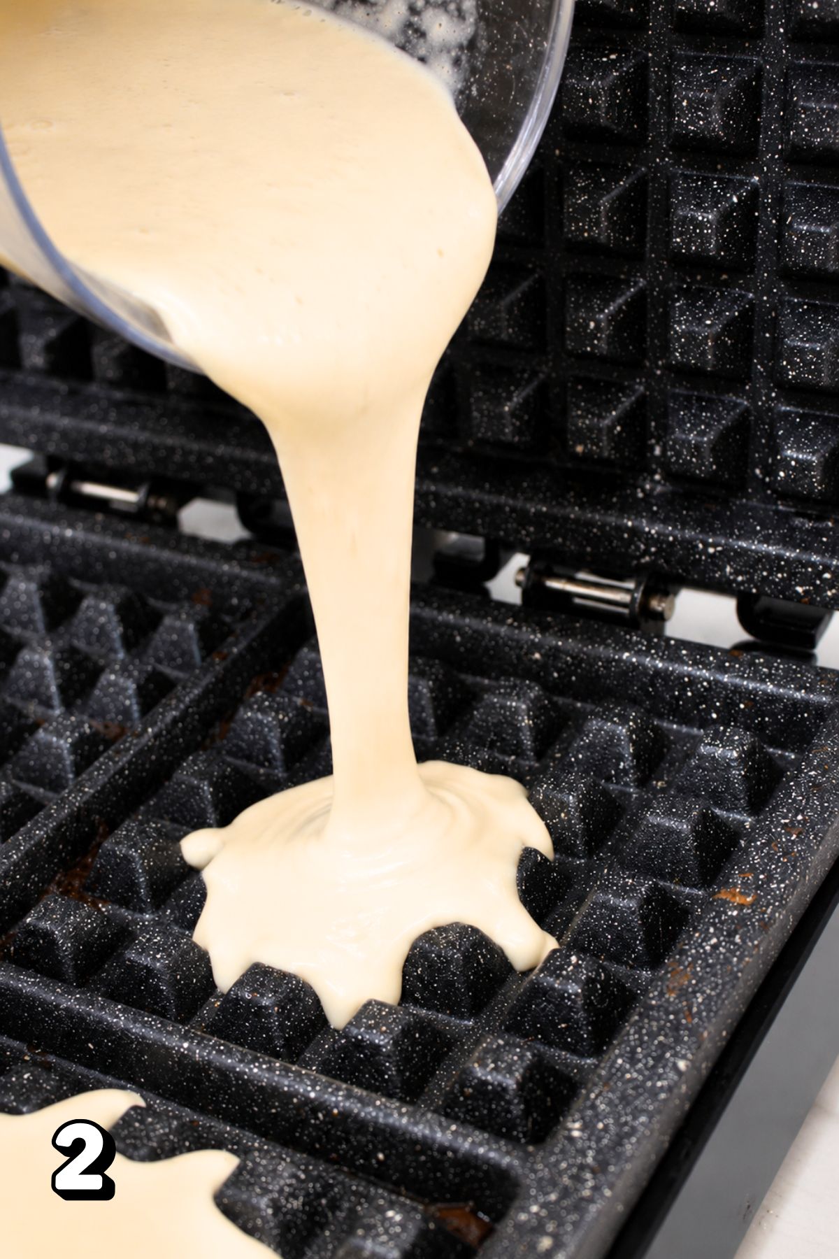 Waffle batter being poured into a cast iron waffle iron.