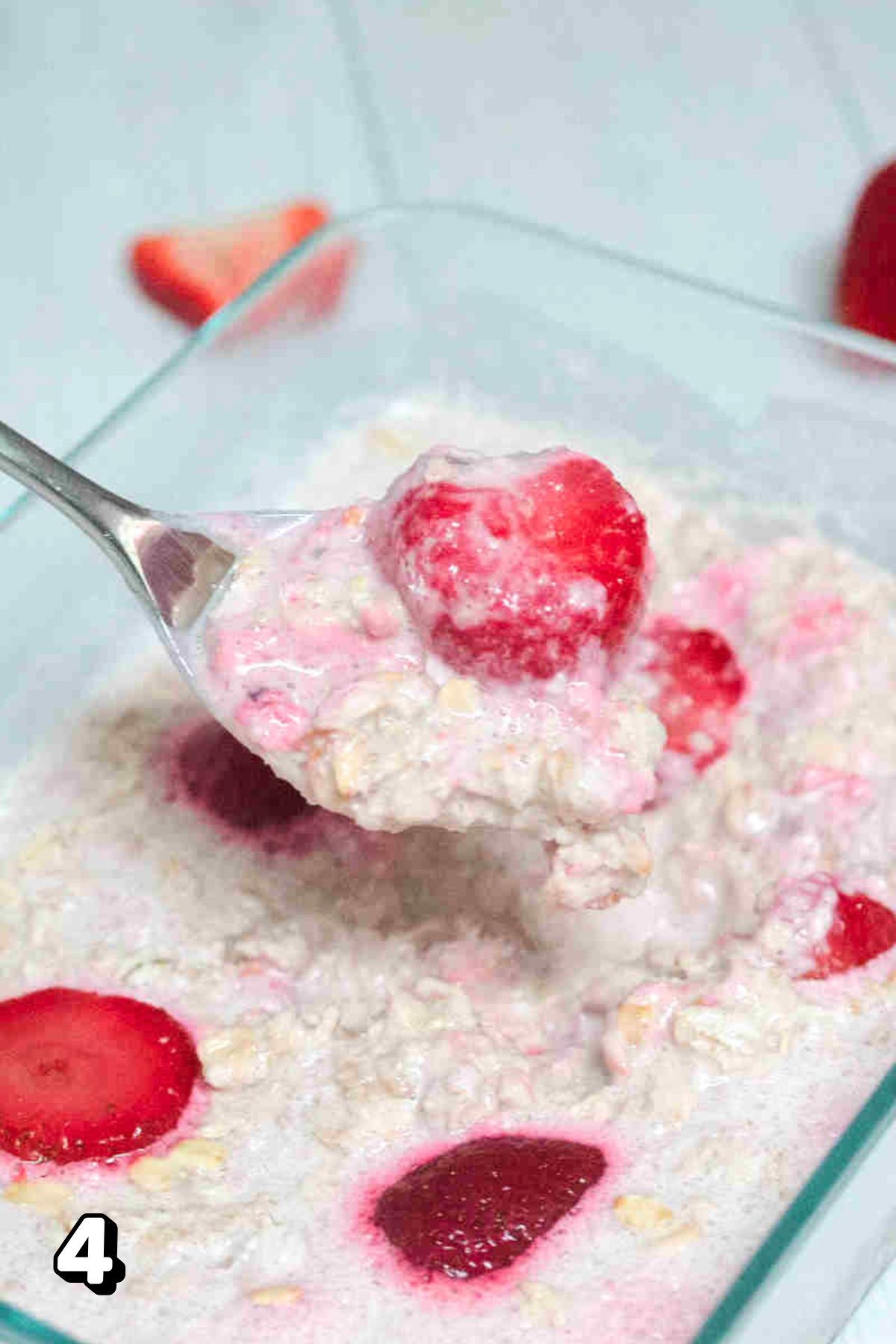 Spoon pulling out overnight oats with strawberries and yogurt.