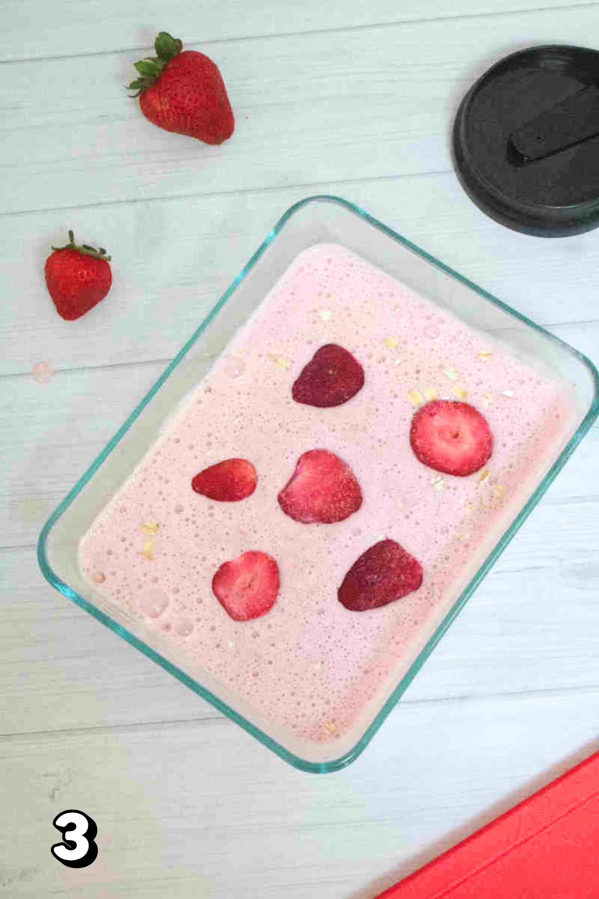 Pink overnight oats with strawberries in a glass container.