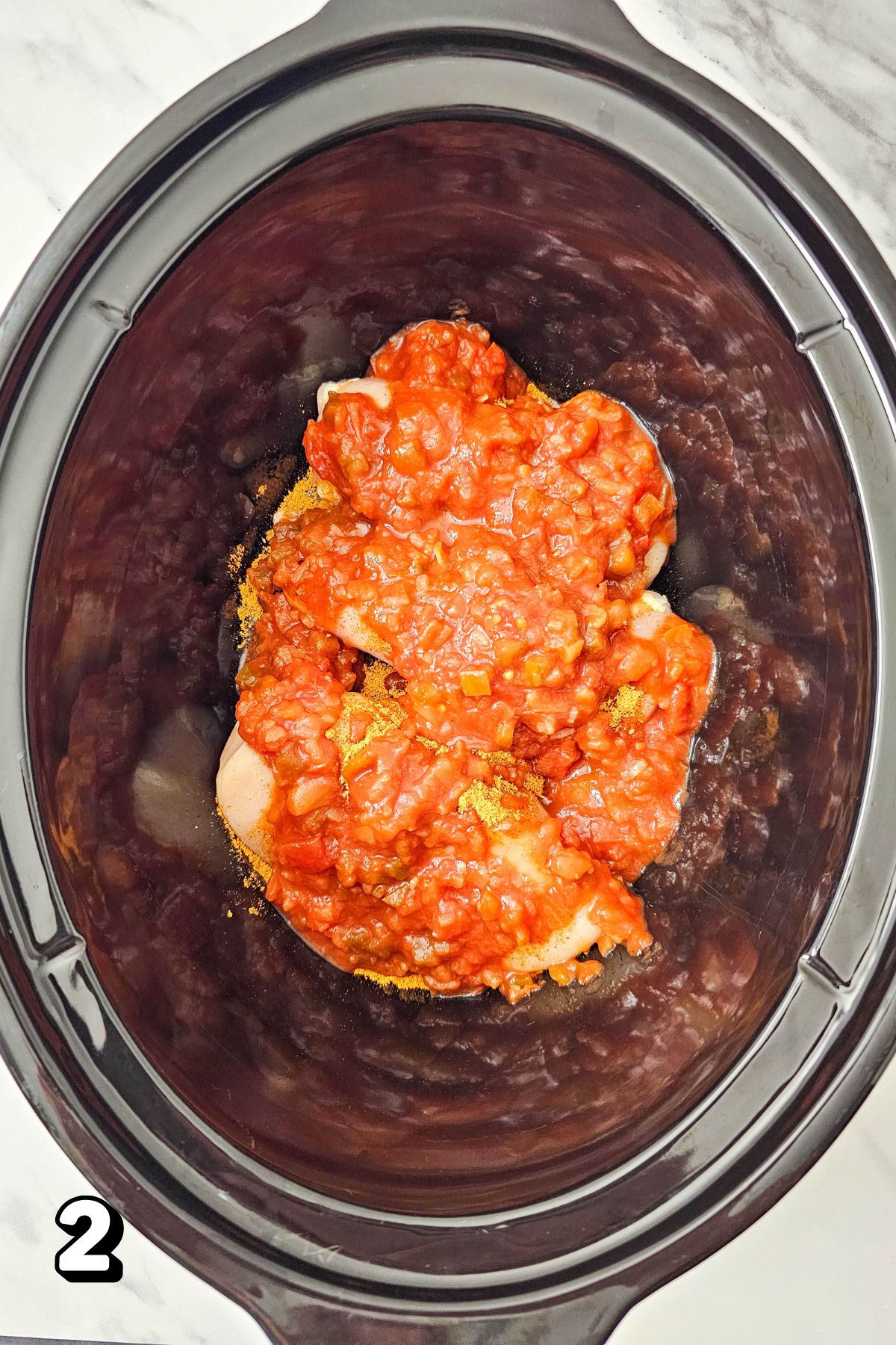Raw chicken breasts with salsa on top in a black slow cooker.