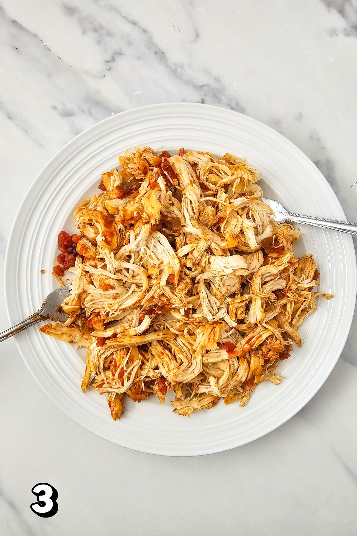 Shredded salsa chicken on a white plate with two forks.