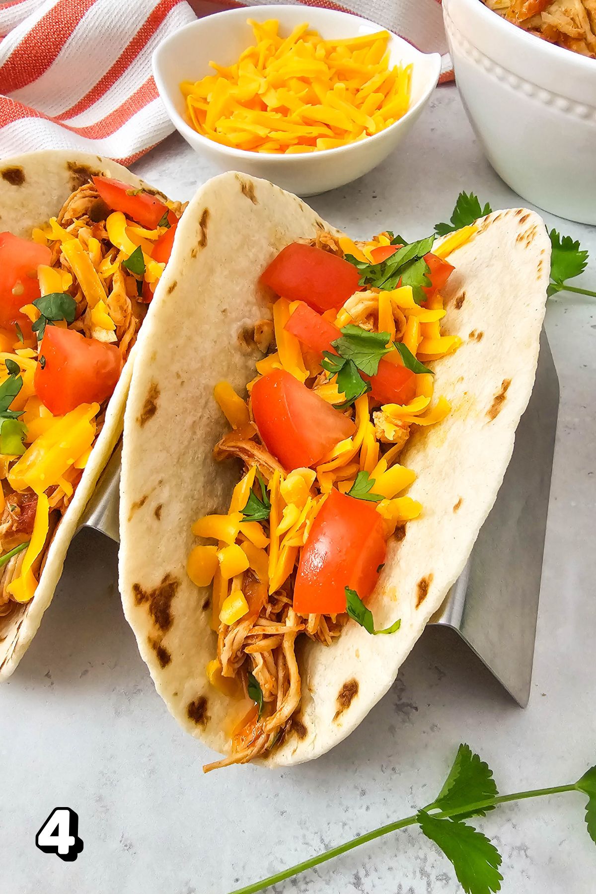 Chicken salsa tacos with tomatoes and cheese and ingredients around them.