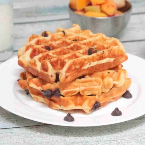 Three chocolate chip waffles stacked on a white plate.