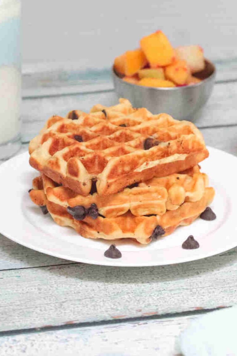 Three chocolate chip waffles stacked on a white plate.