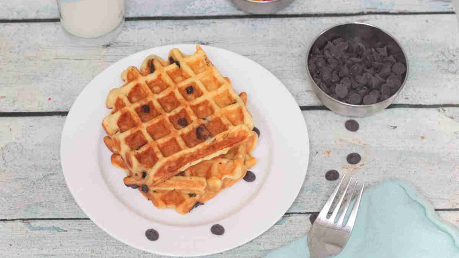 Three chocolate chip waffles stacked on a white plate.