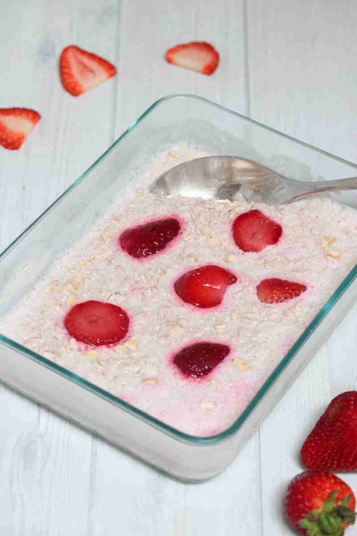 Pink overnight oats with strawberries in a glass container with a spoon in it.