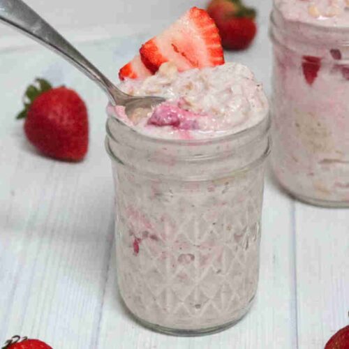 Two jars with blended yogurt overnight oats with strawberries and one jar has a spoon in it.