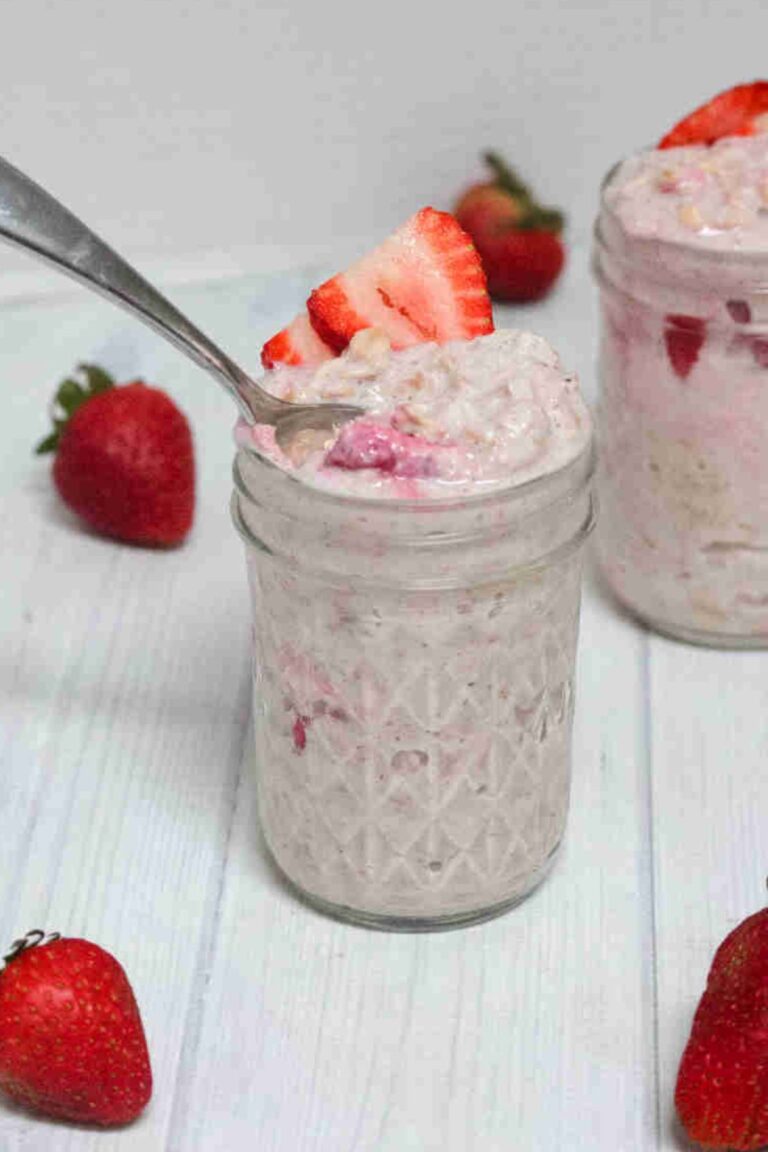 Two jars with blended yogurt overnight oats with strawberries and one jar has a spoon in it.