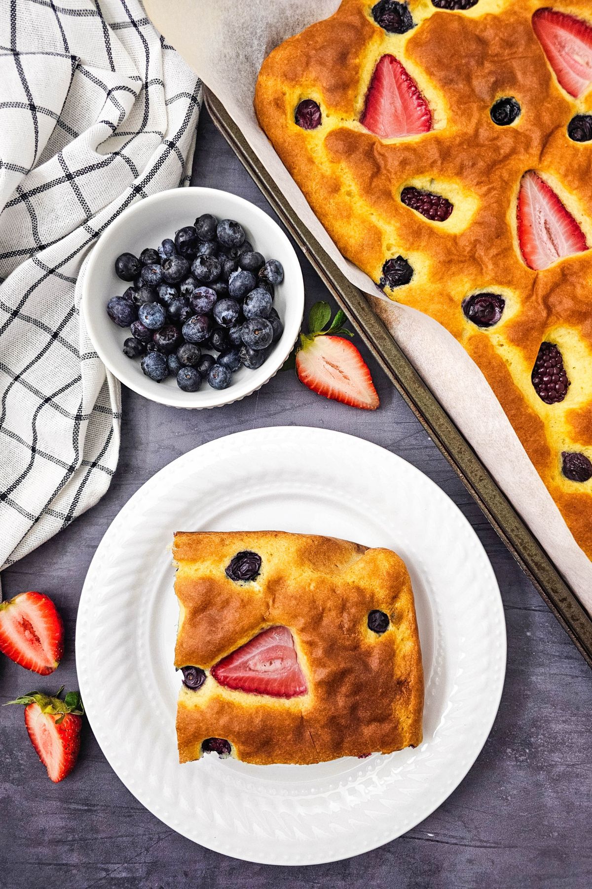 Sheet pan berry pancakes with a plate with one pancake beside it.