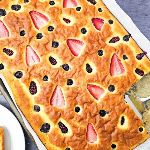 Sheet pan pancakes with berries on a baking sheet with one slice cut out.