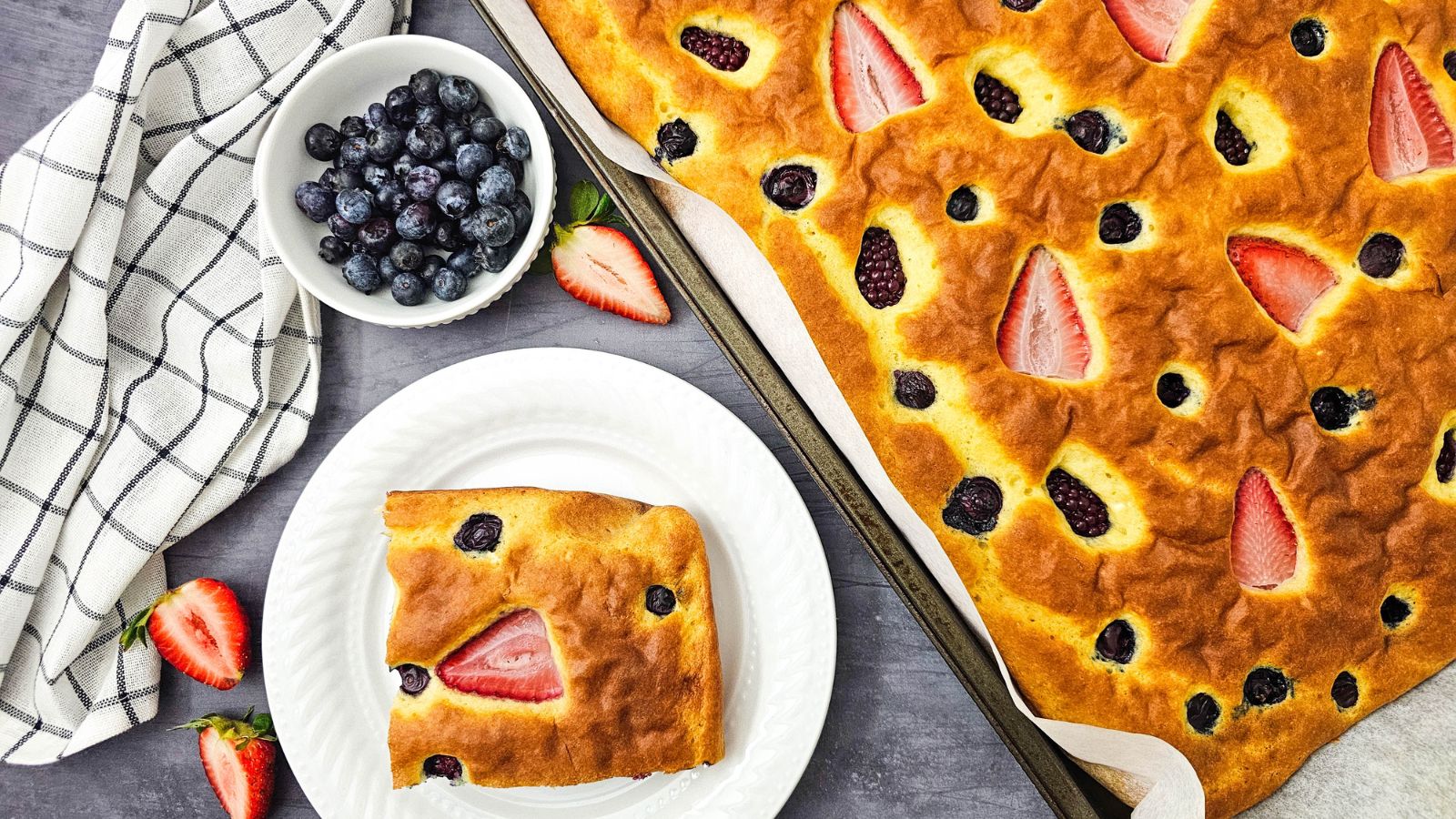 Sheet pan berry pancakes with a plate with one pancake beside it.