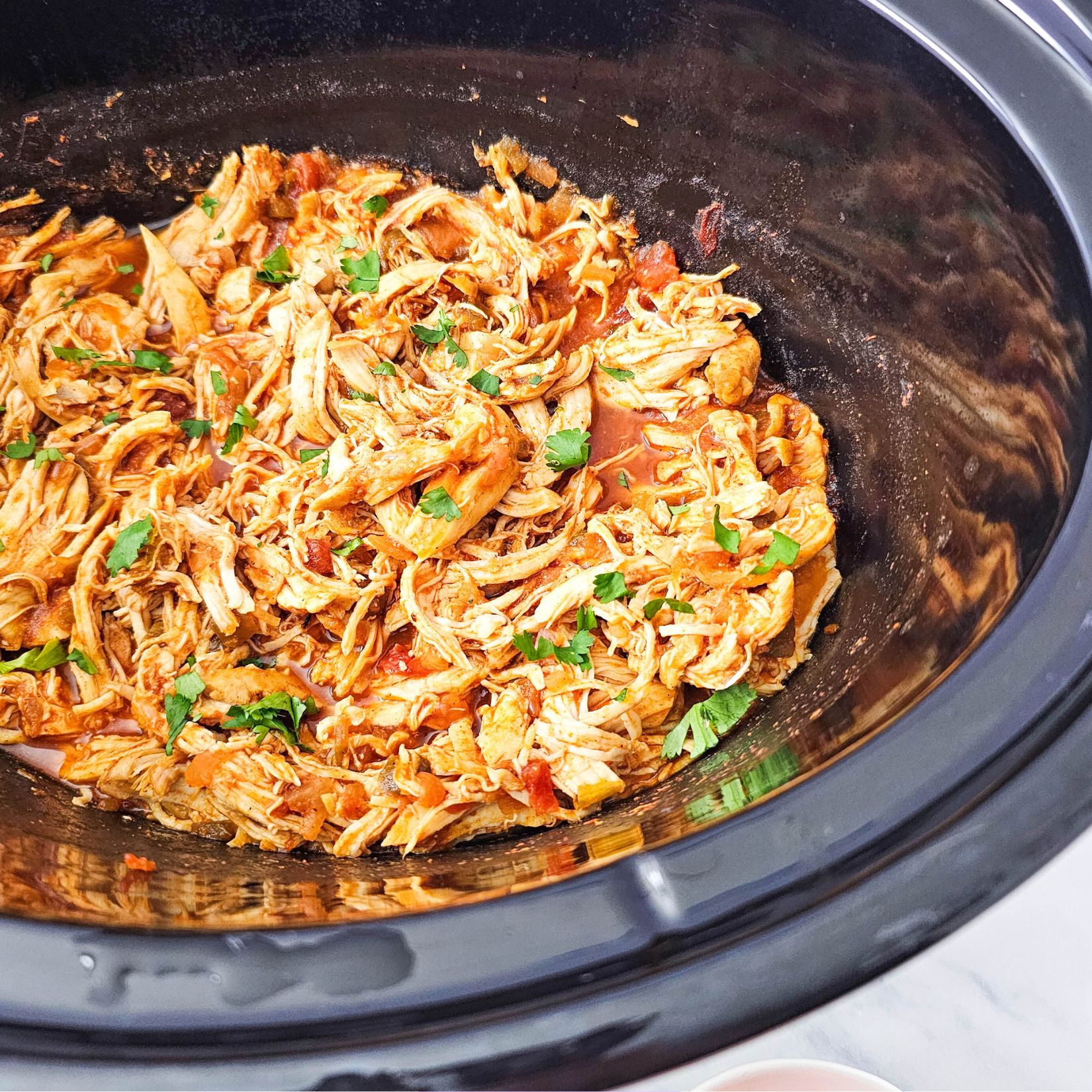 Shredded salsa chicken in a black crockpot.