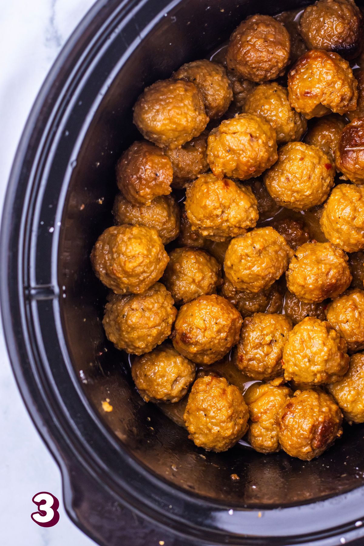Mongolian meatballs stacked in a black slow cooker.