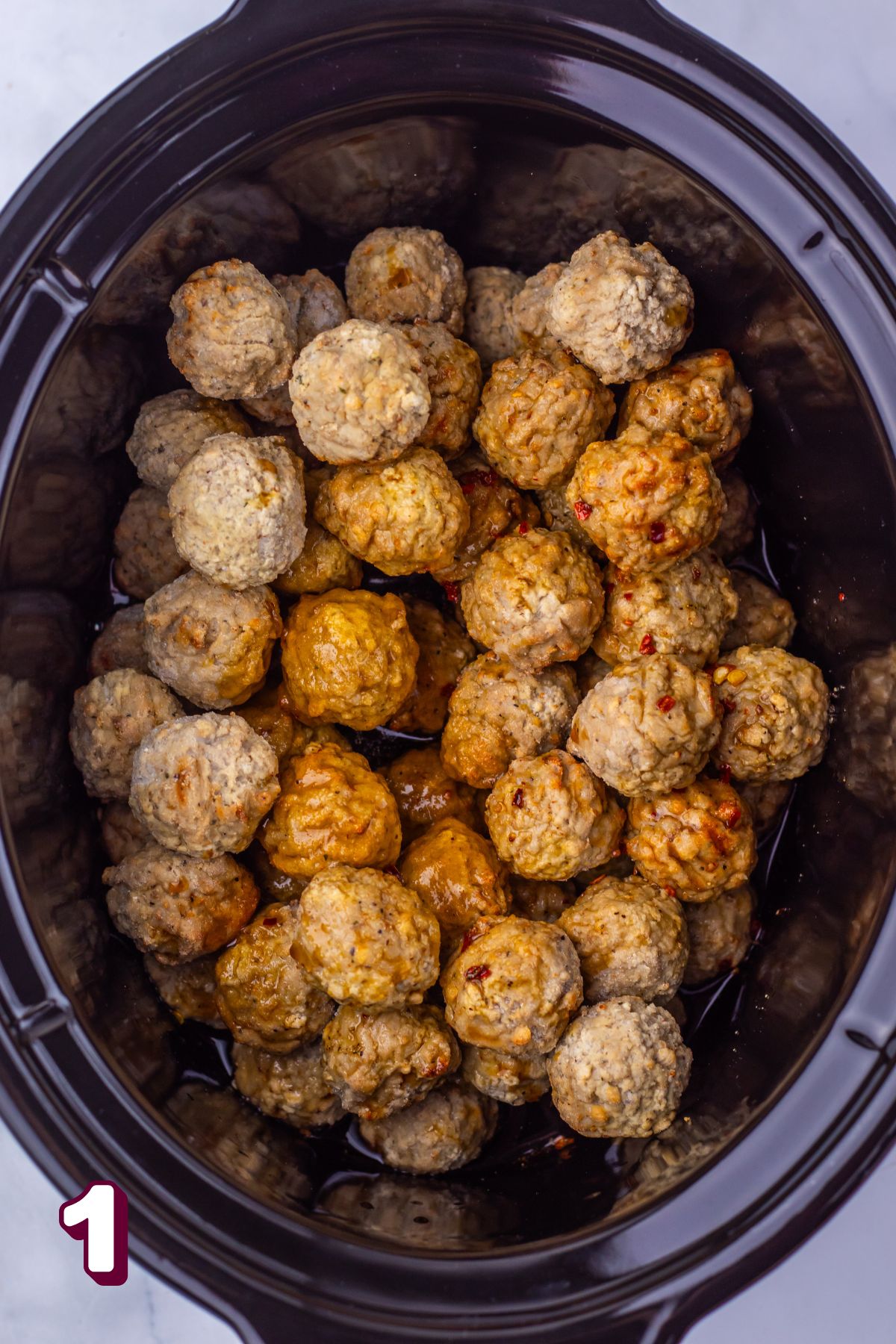 Black slow cooker with frozen meatballs in it.