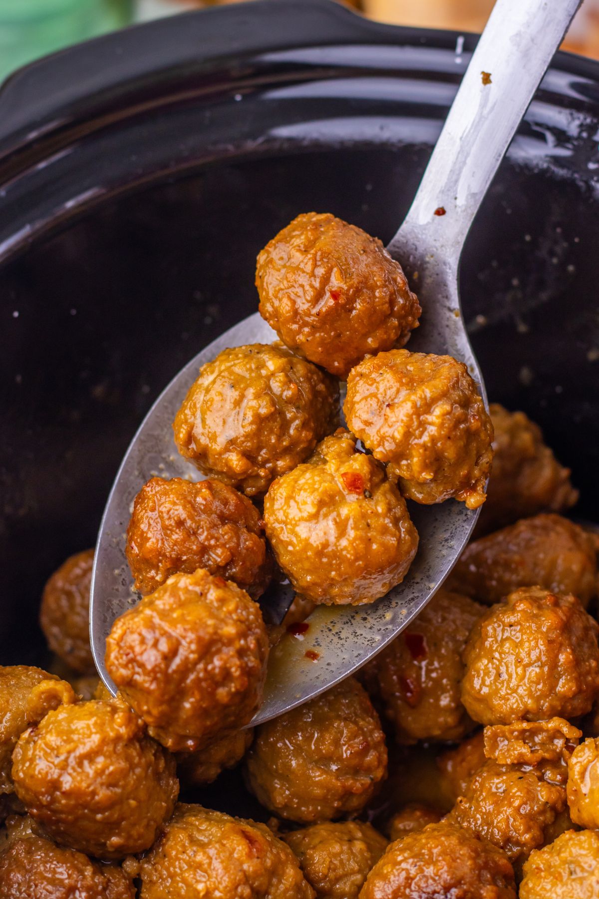 Mongolian meatballs in a black slow cooker with a metal spoon.