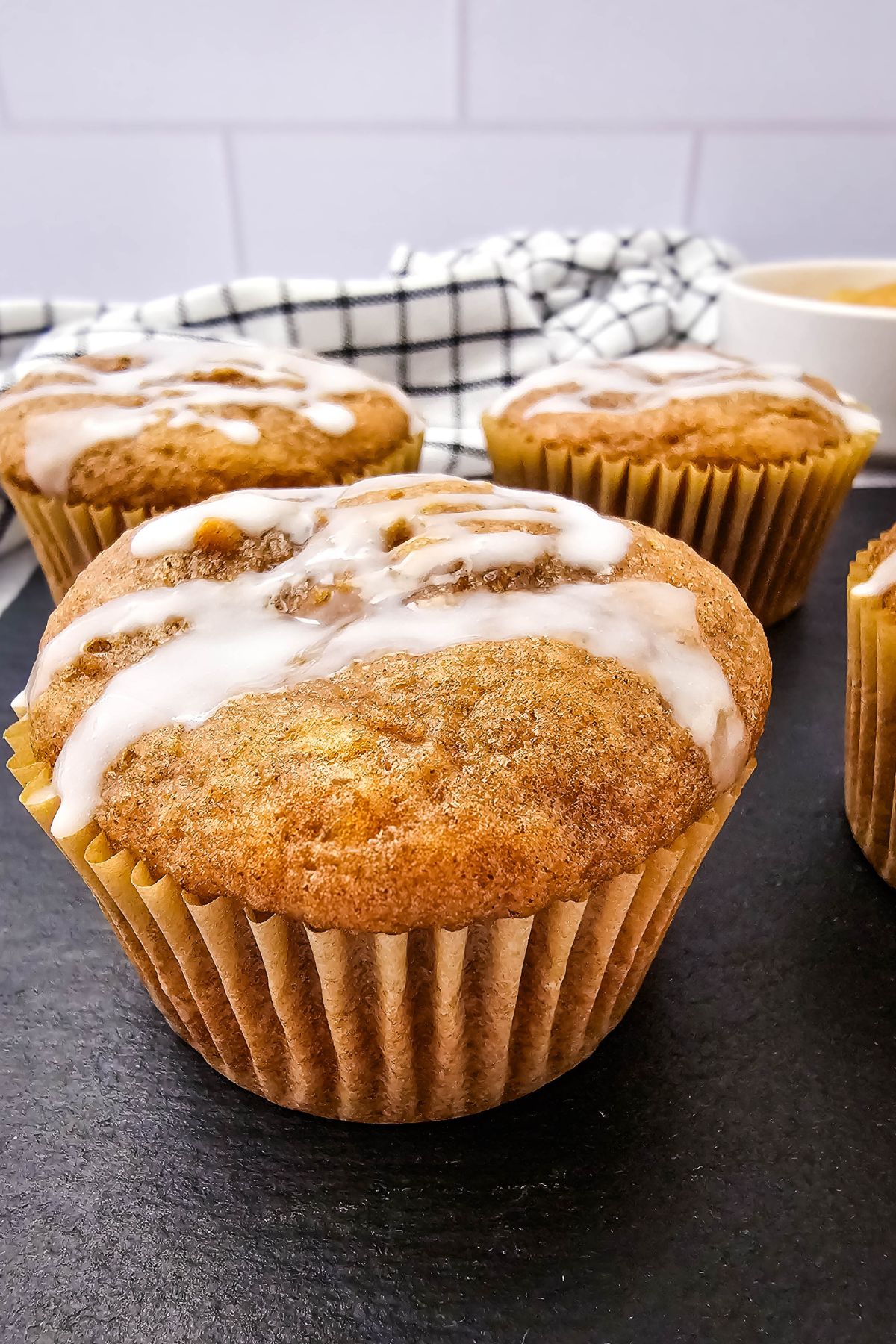 Apple pie muffin with sweet glaze on top and more muffins behind it.