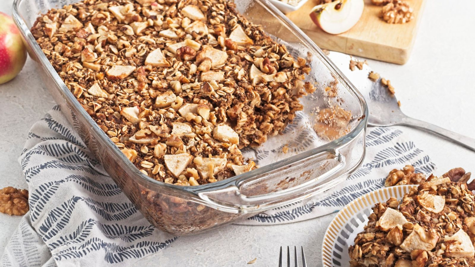 Baked apple oatmeal topped with apples in a glass baking dish with a slice on a plate beside it.