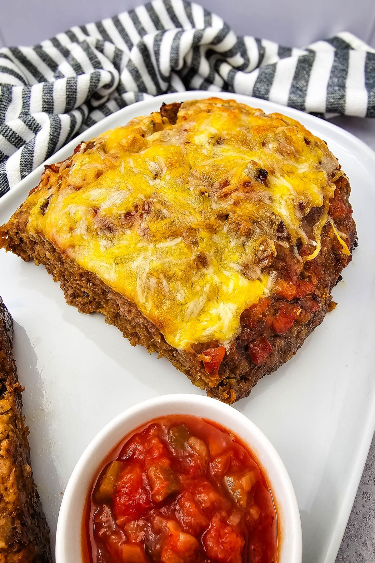 Cheesy salsa meatloaf cut in half on a plate with a bowl of salsa beside it.