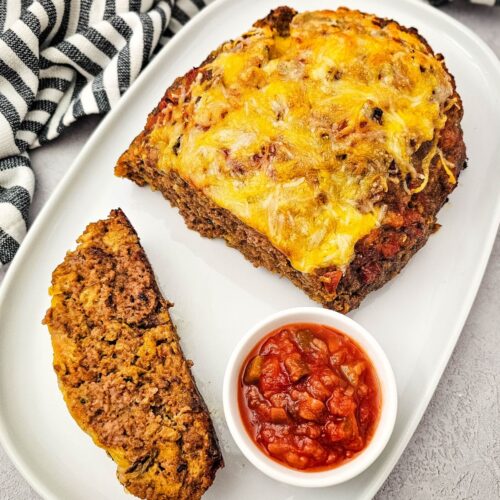 Cheesy salsa meatloaf cut in half on a plate with a bowl of salsa beside it.