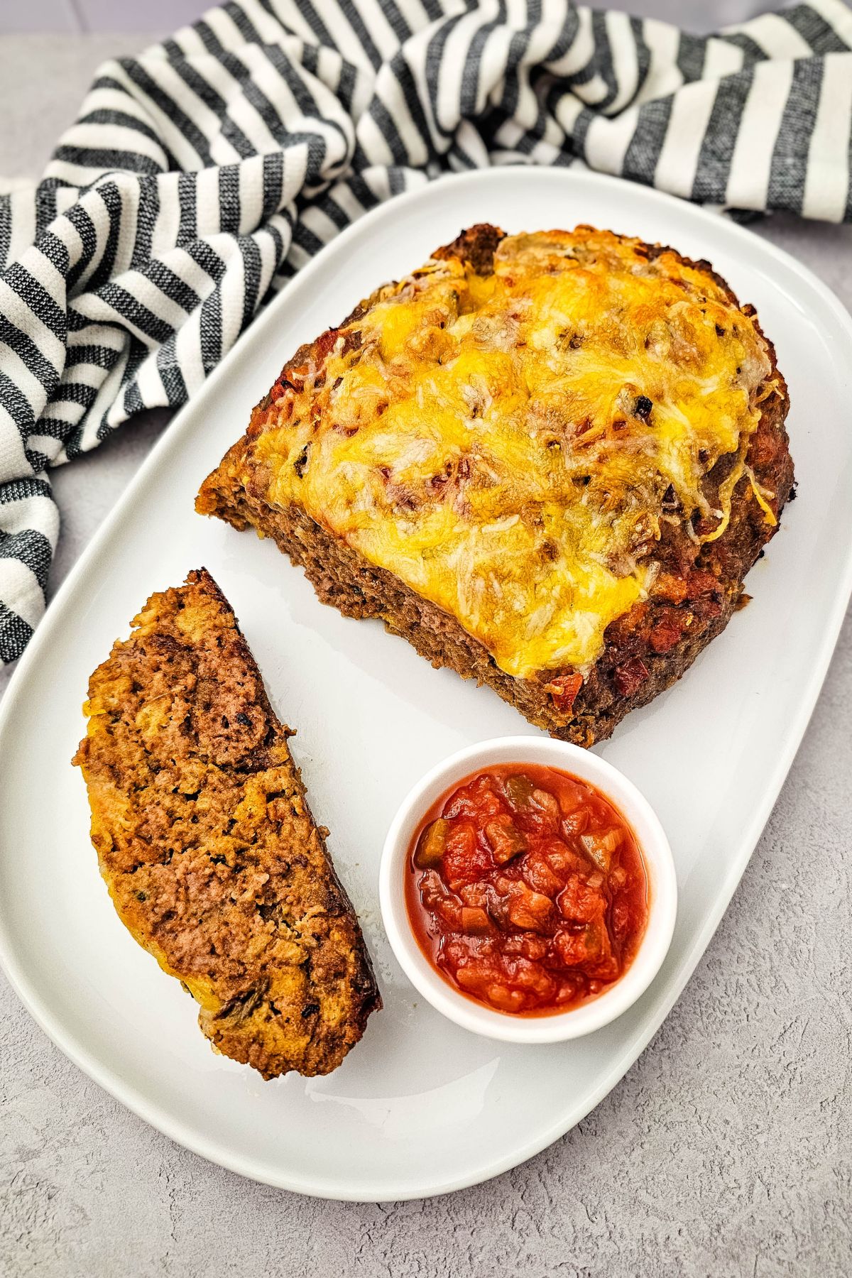 Cheesy salsa meatloaf cut in half on a plate with a bowl of salsa beside it.