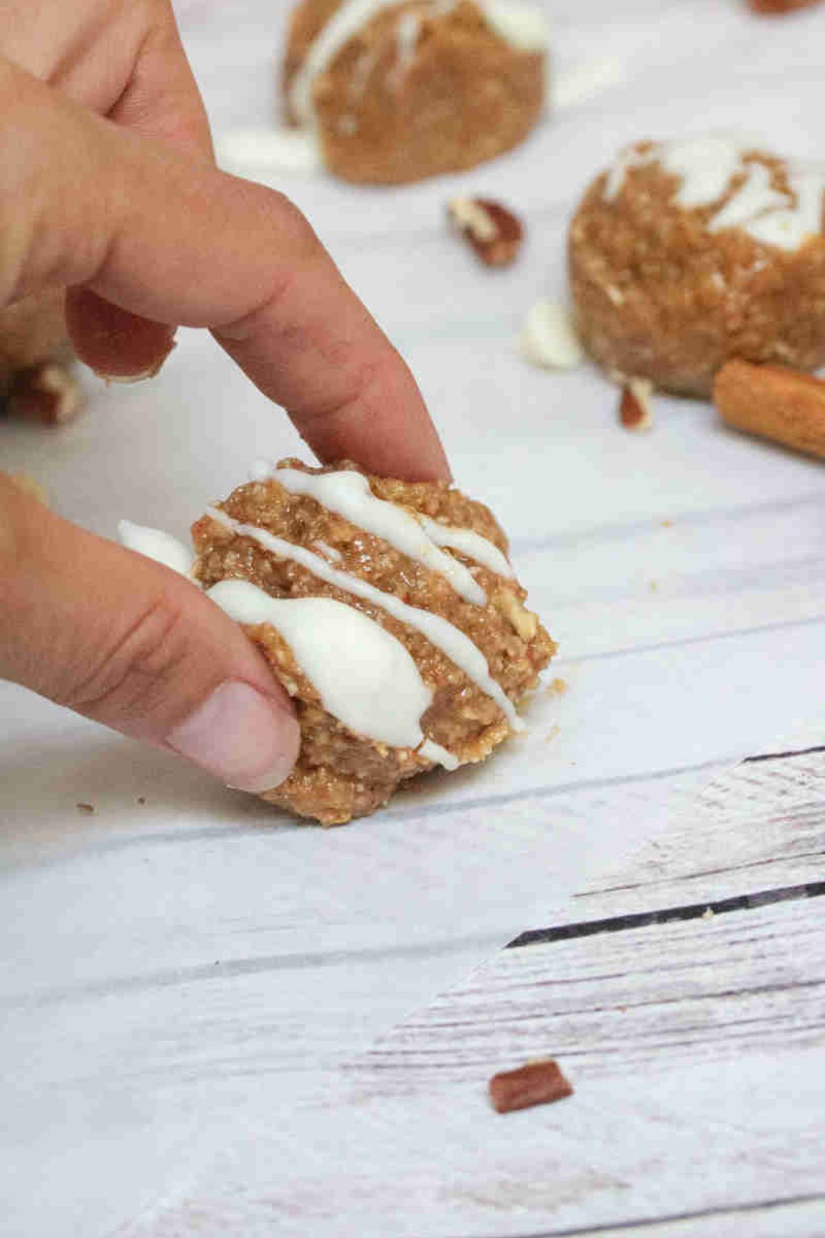Two fingers placing a cinnamon energy ball with white chocolate on top on parchment paper.