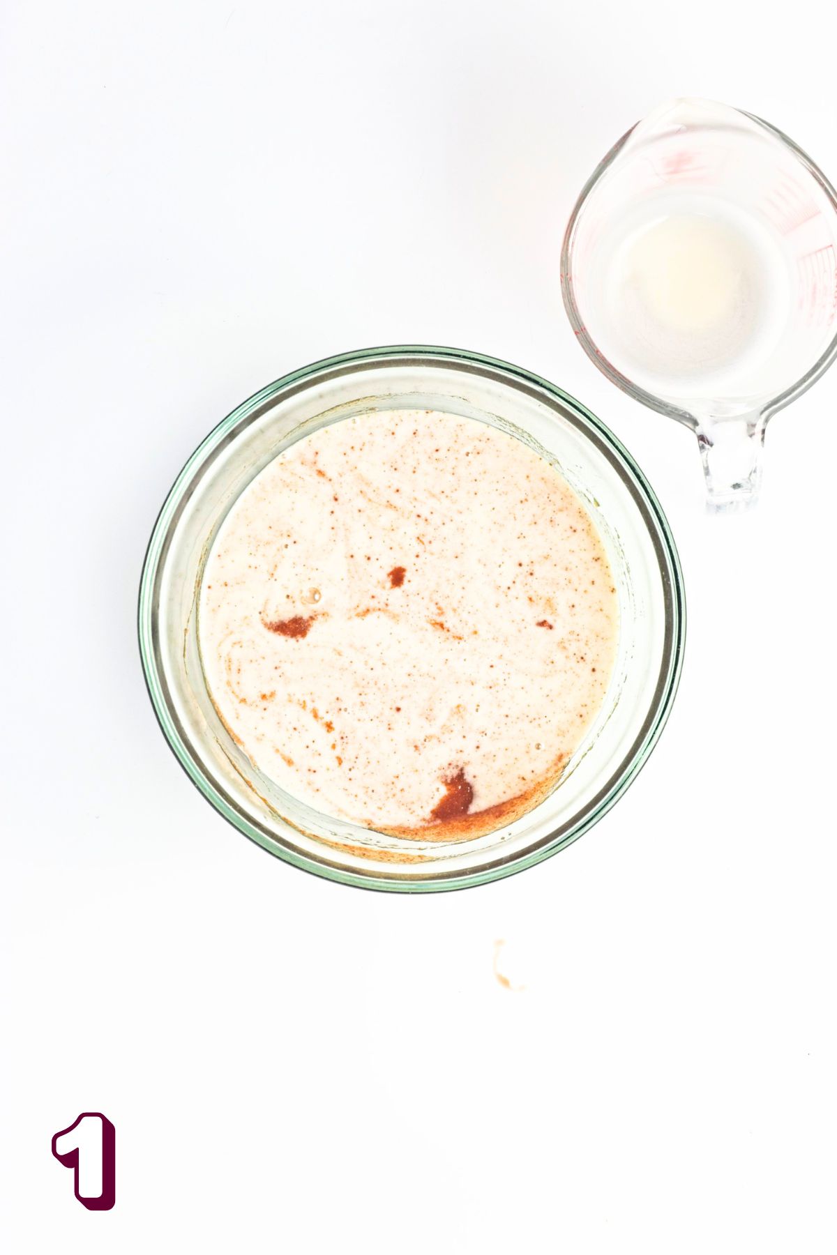 Glass bowl with milk and maple syrup in it and a measuring cup beside it.
