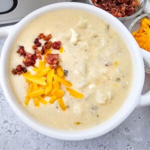 White bowl with loaded baked potato soup topped with cheese and bacon.