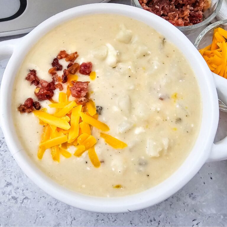 White bowl with loaded baked potato soup topped with cheese and bacon.