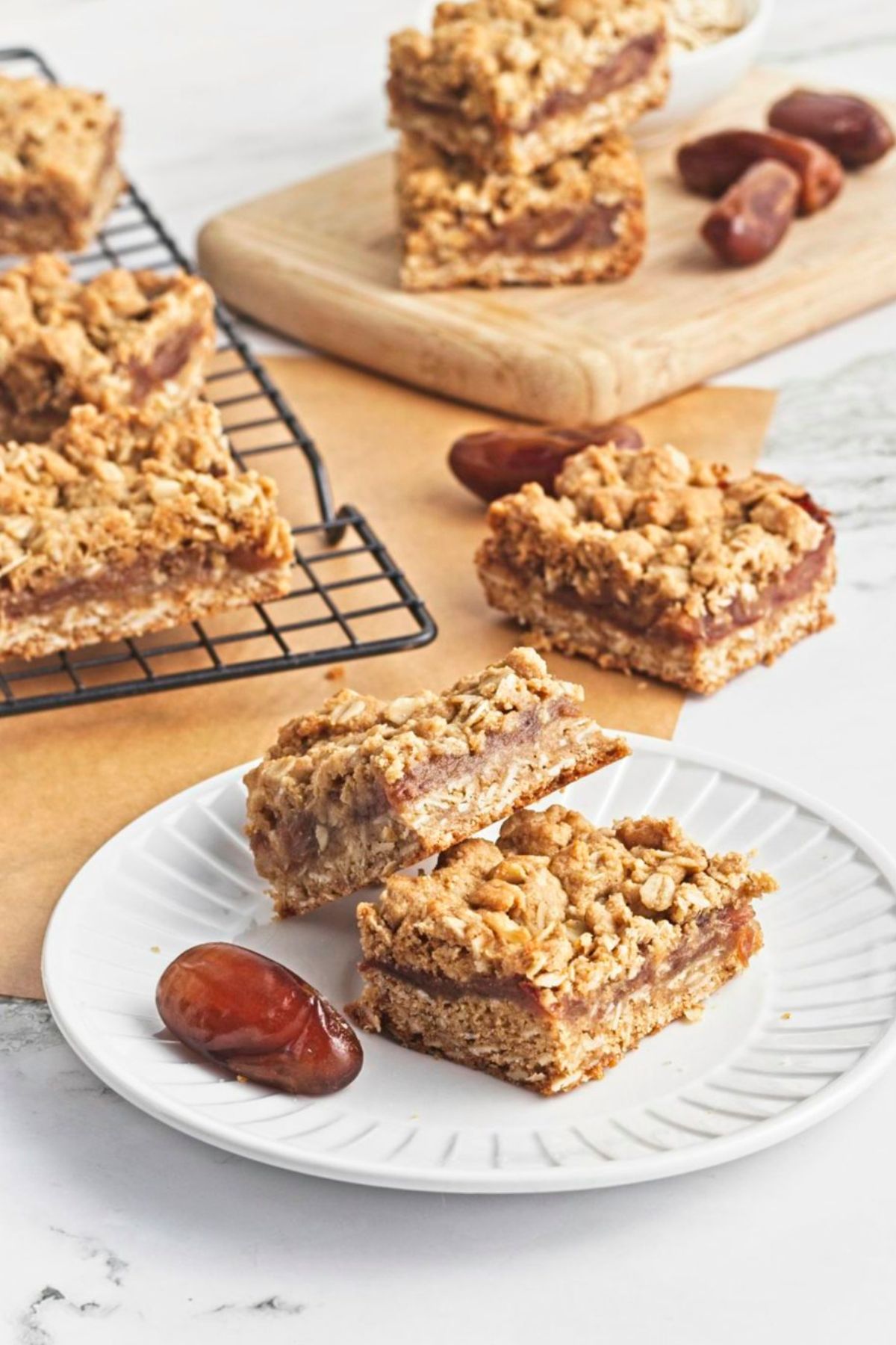 Two date and oat squares stacked on a white plate with dates and more squares around them.