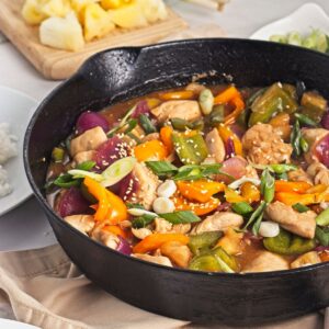 Pineapple chicken dinner with bell peppers in a cast iron pan.
