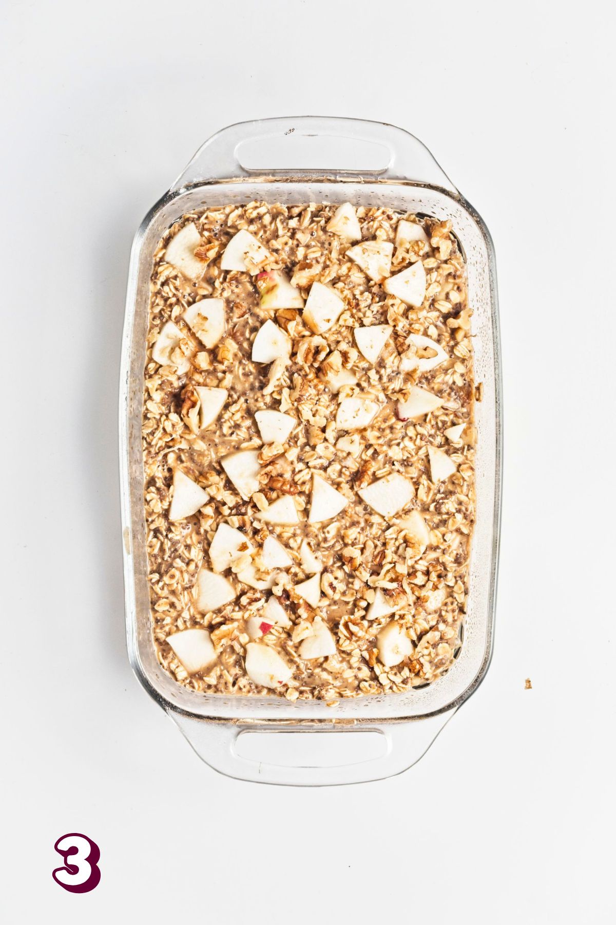 Uncooked apple baked oatmeal topped with chopped apples in a glass baking dish.