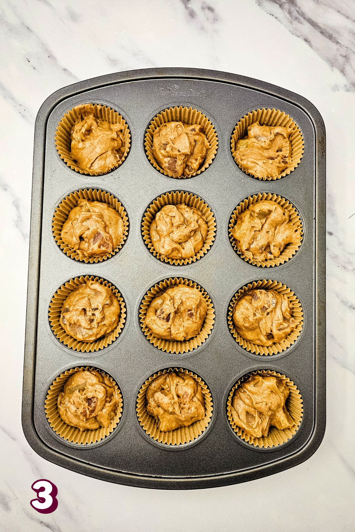 Raw apple pie muffins in cupcake liners in a pan.