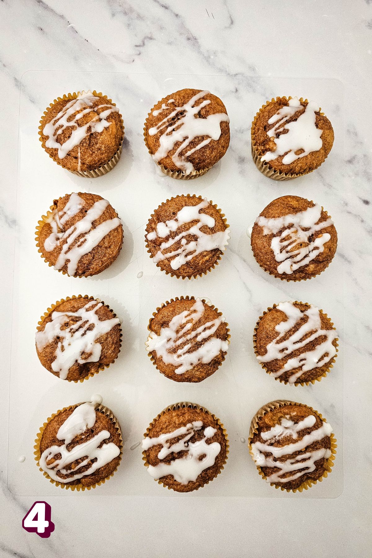 Apple pie muffins with icing glaze on top all lined up on a marble counter.