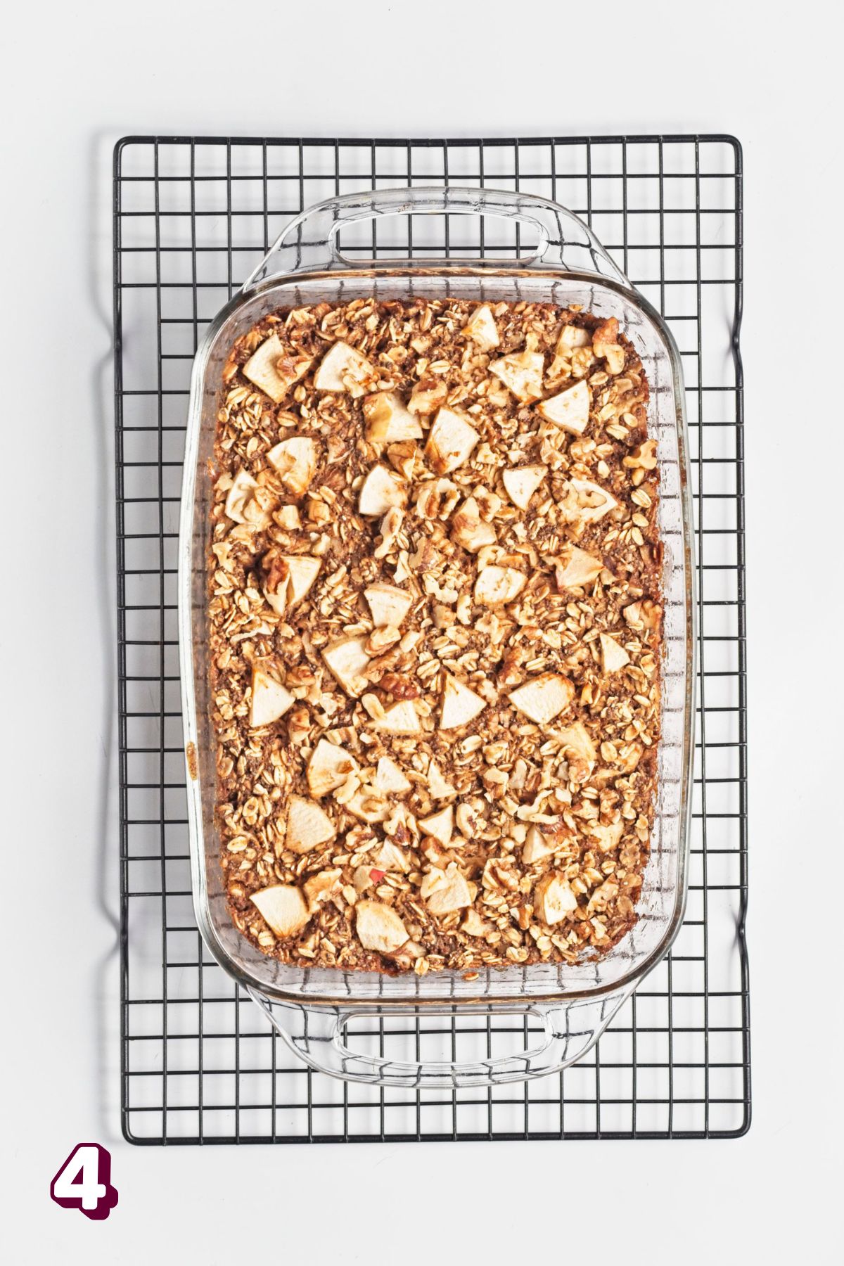 Apple baked oatmeal topped with chopped apples in a glass baking dish on a cooling rack.