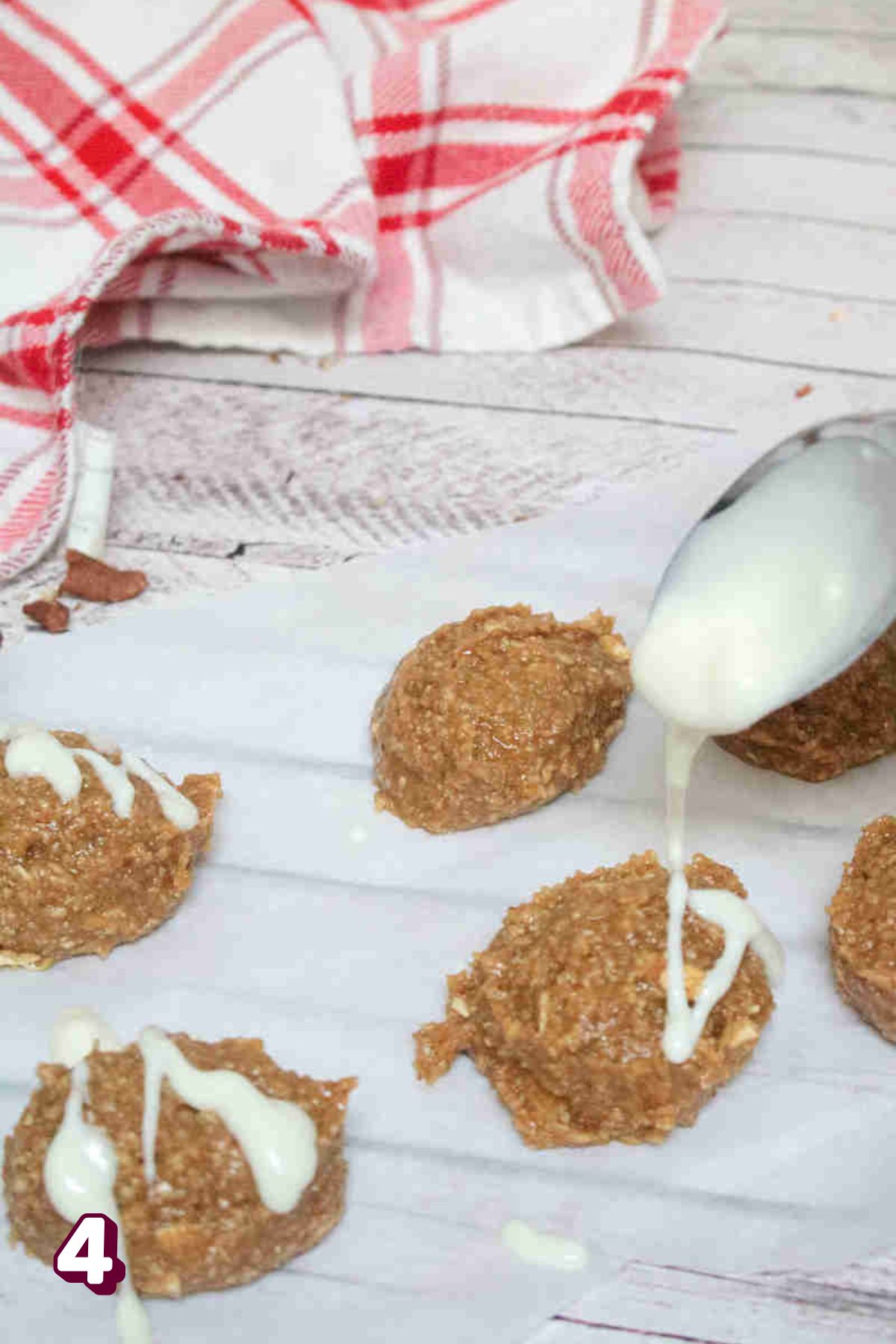 White chocolate being poured onto no bake cinnamon energy balls on parchment paper.