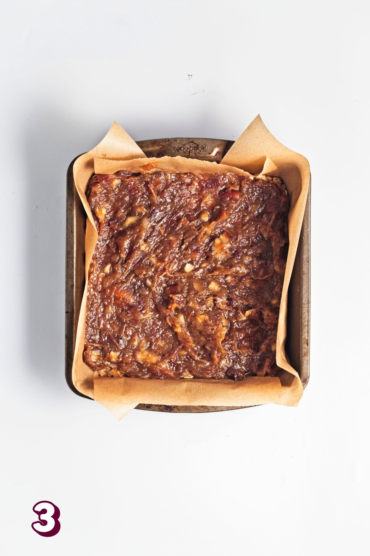 Date filling on top of an oatmeal base in a baking dish lined with parchment paper.