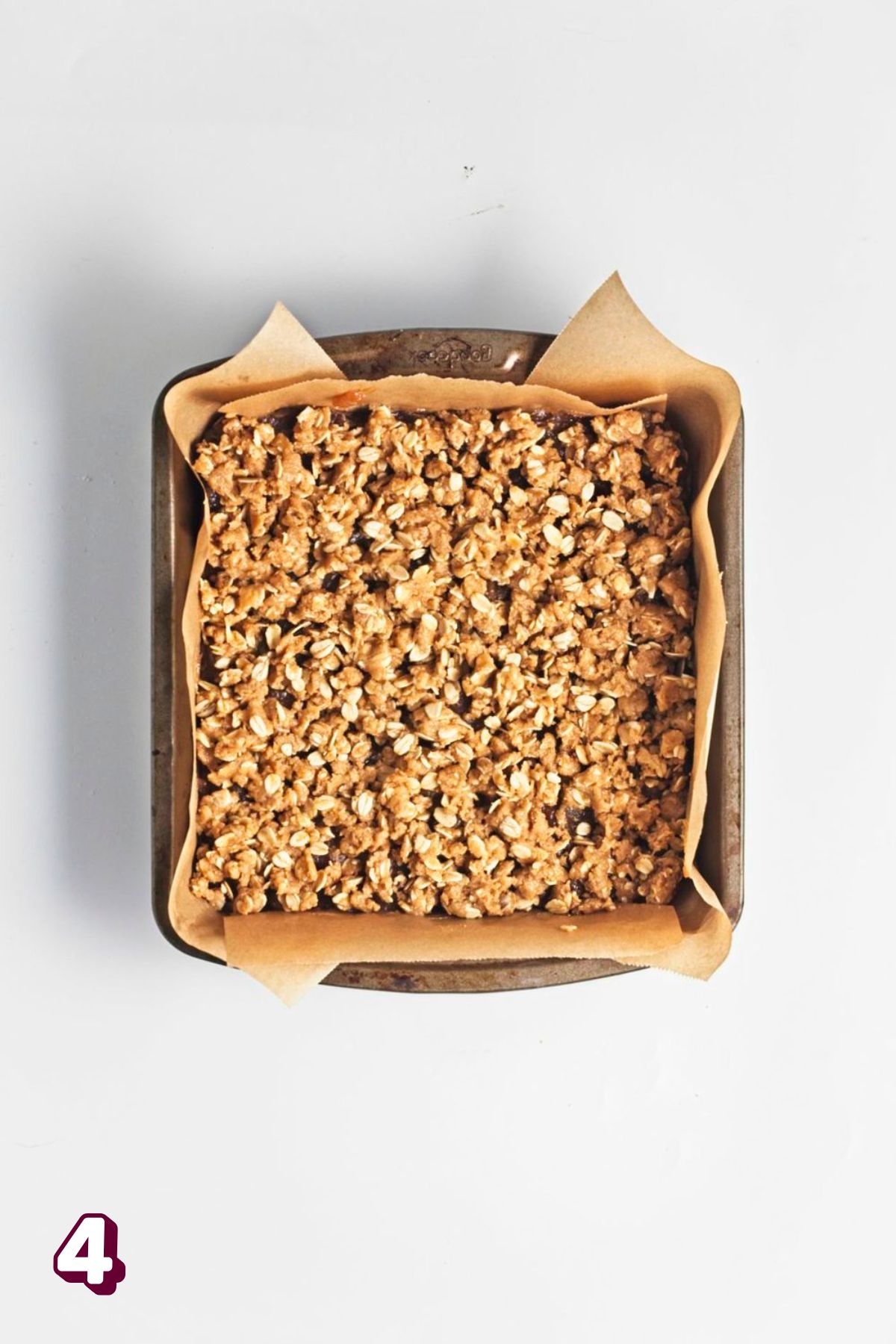 Oat crumble on top of date filling in a parchment paper lined baking dish.