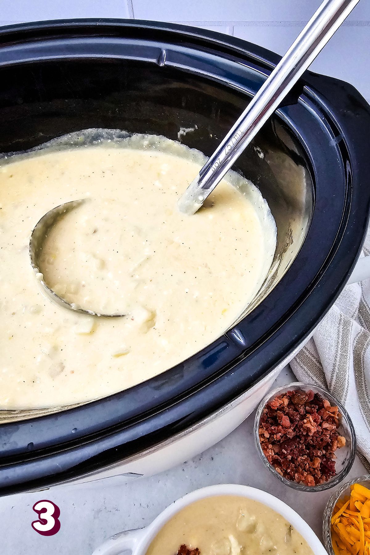 A crockpot with loaded potato soup in it and a ladle.