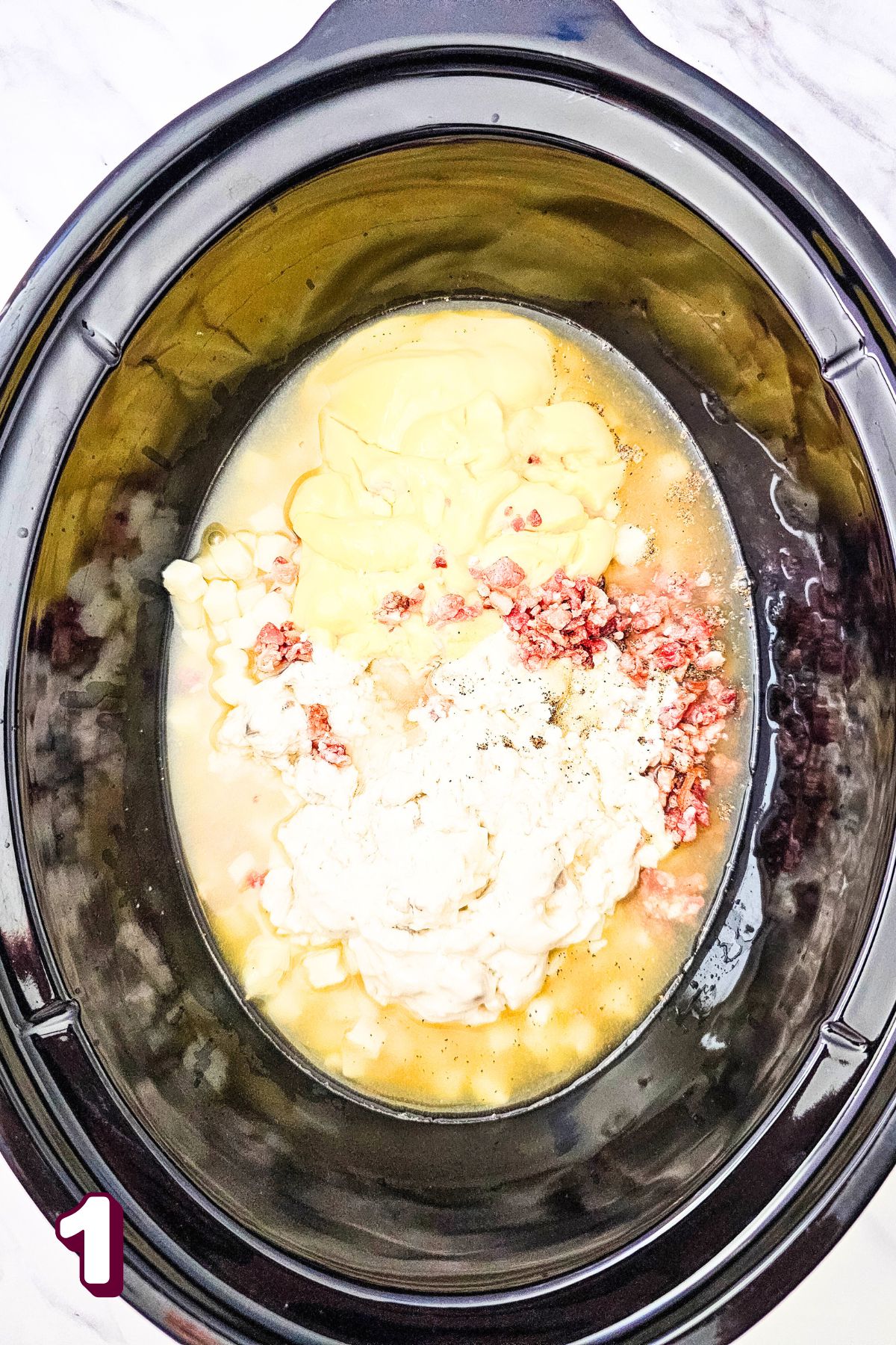 Black crockpot with broth, soups, bacon bits, and hashbrowns in it.