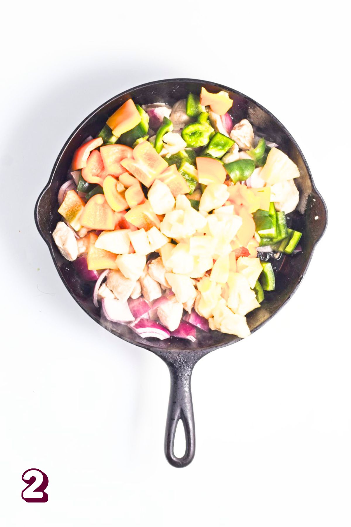 Chicken, pineapple, ad bell peppers in a cast iron pan.