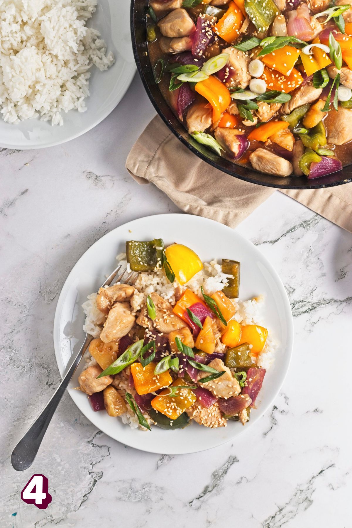White plate with chicken pineapple stir fry on rice and more in a cast iron skillet behind.