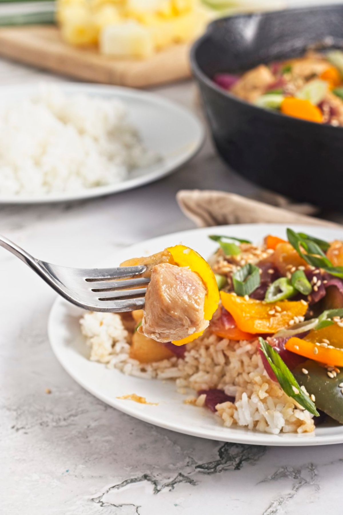 Pineapple chicken dinner with bell peppers over rice on a white plate with a fork pulling out chicken.