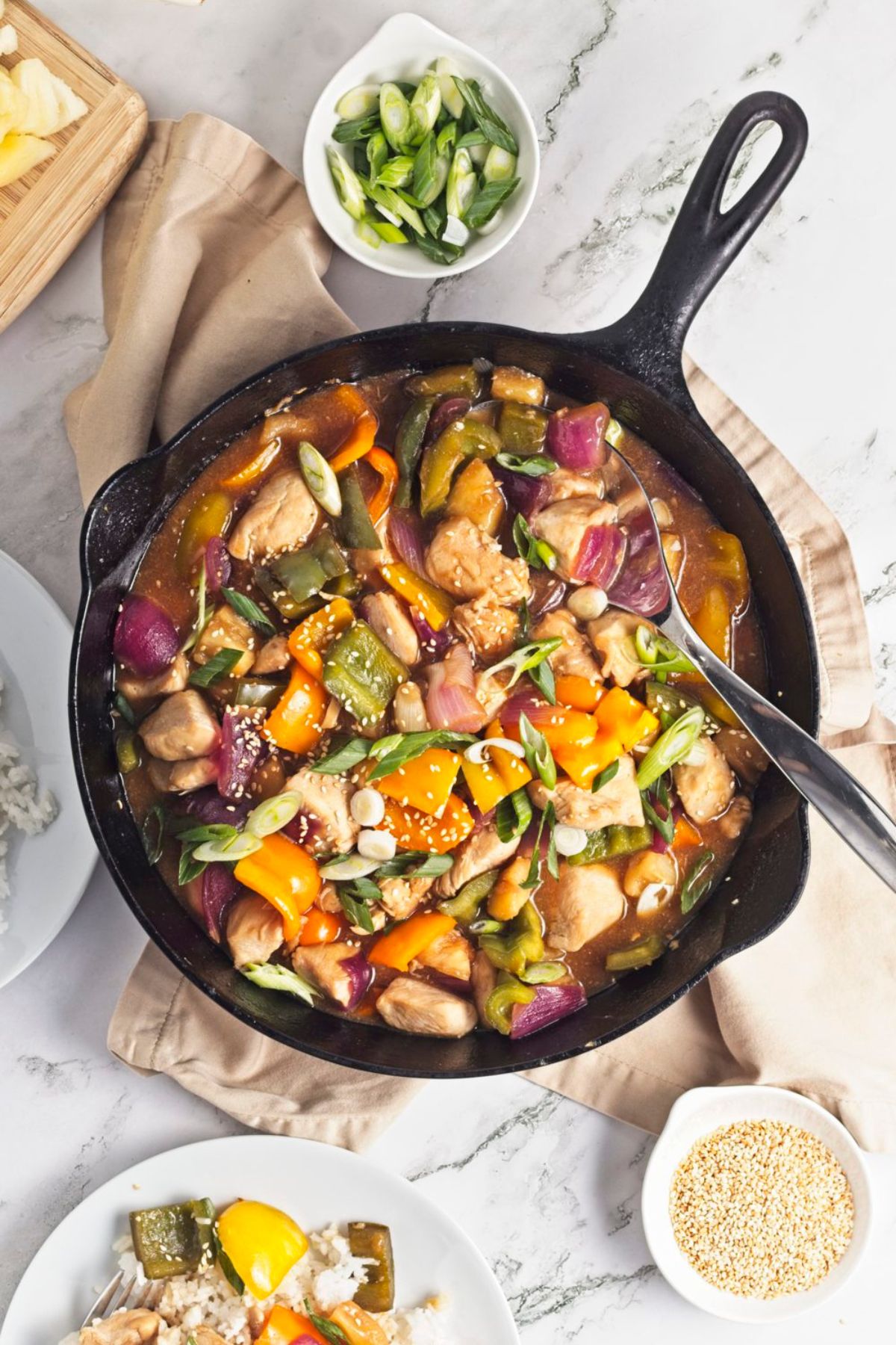 Pineapple chicken dinner with bell peppers in a cast iron pan surrounded by ingredients.
