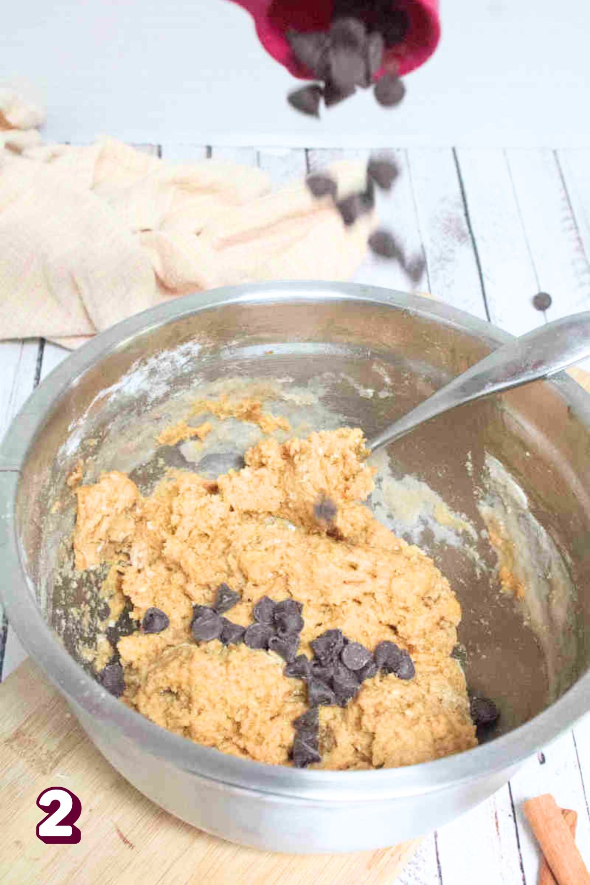 Raw pumpkin chocolate chip cookie batter in a steel bowl being mixed and chocolate chips being added.