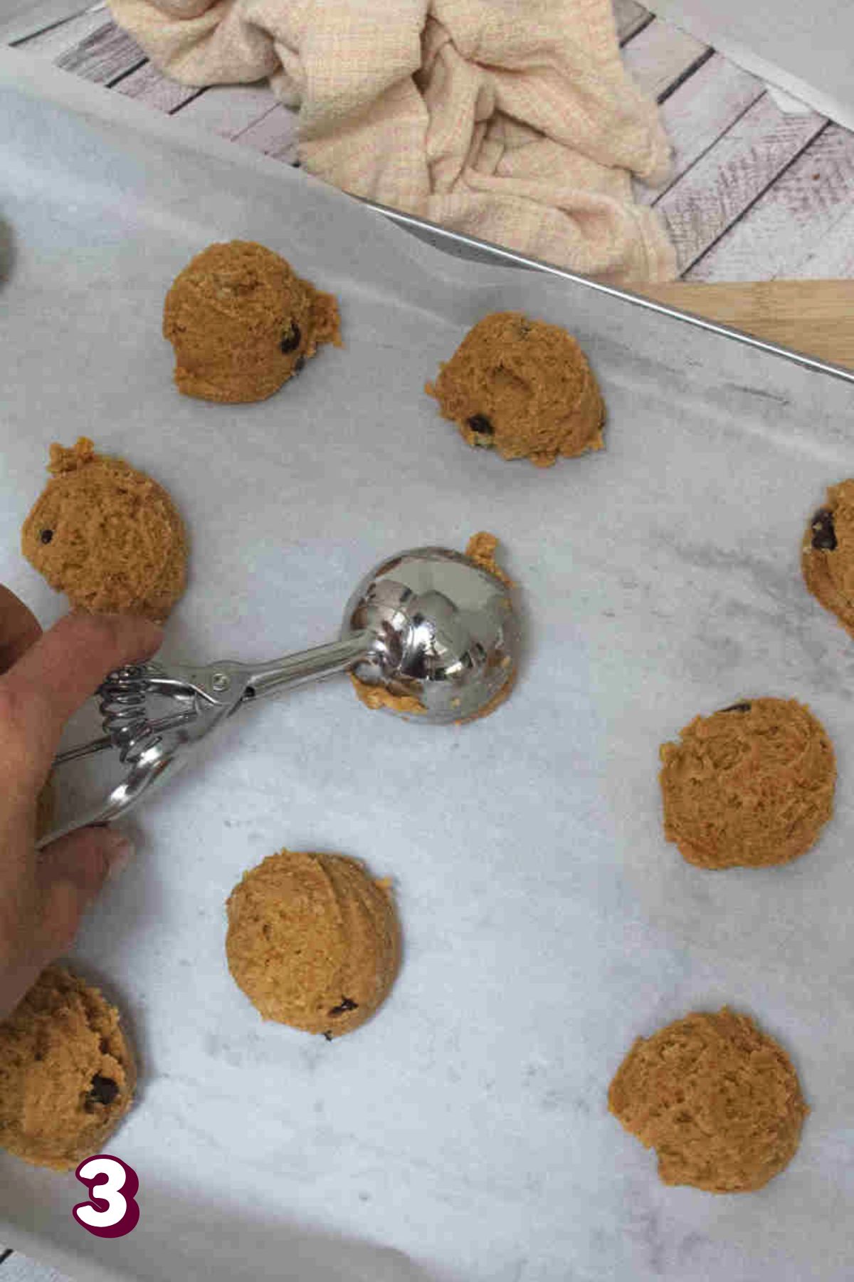 Raw pumpkin chocolate chip cookie batter being portioned onto a lined baking sheet.