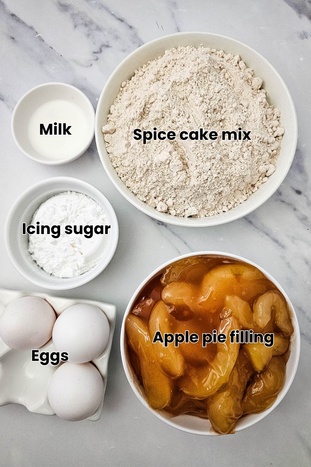 Cake mix, canned apples, icing sugar, eggs, and milk in bowls with text labels on top.