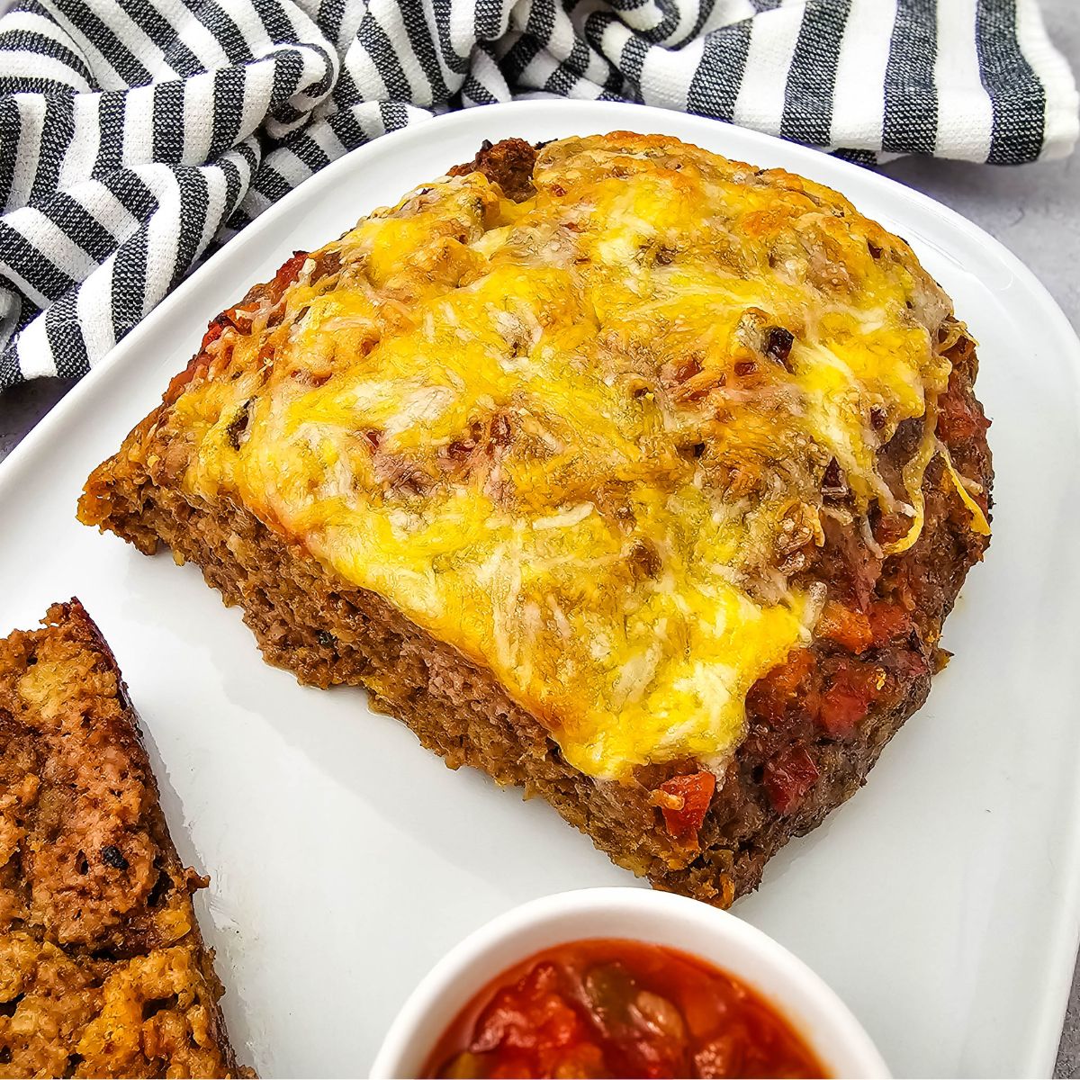 Cheesy salsa meatloaf cut in half on a plate with a bowl of salsa beside it.