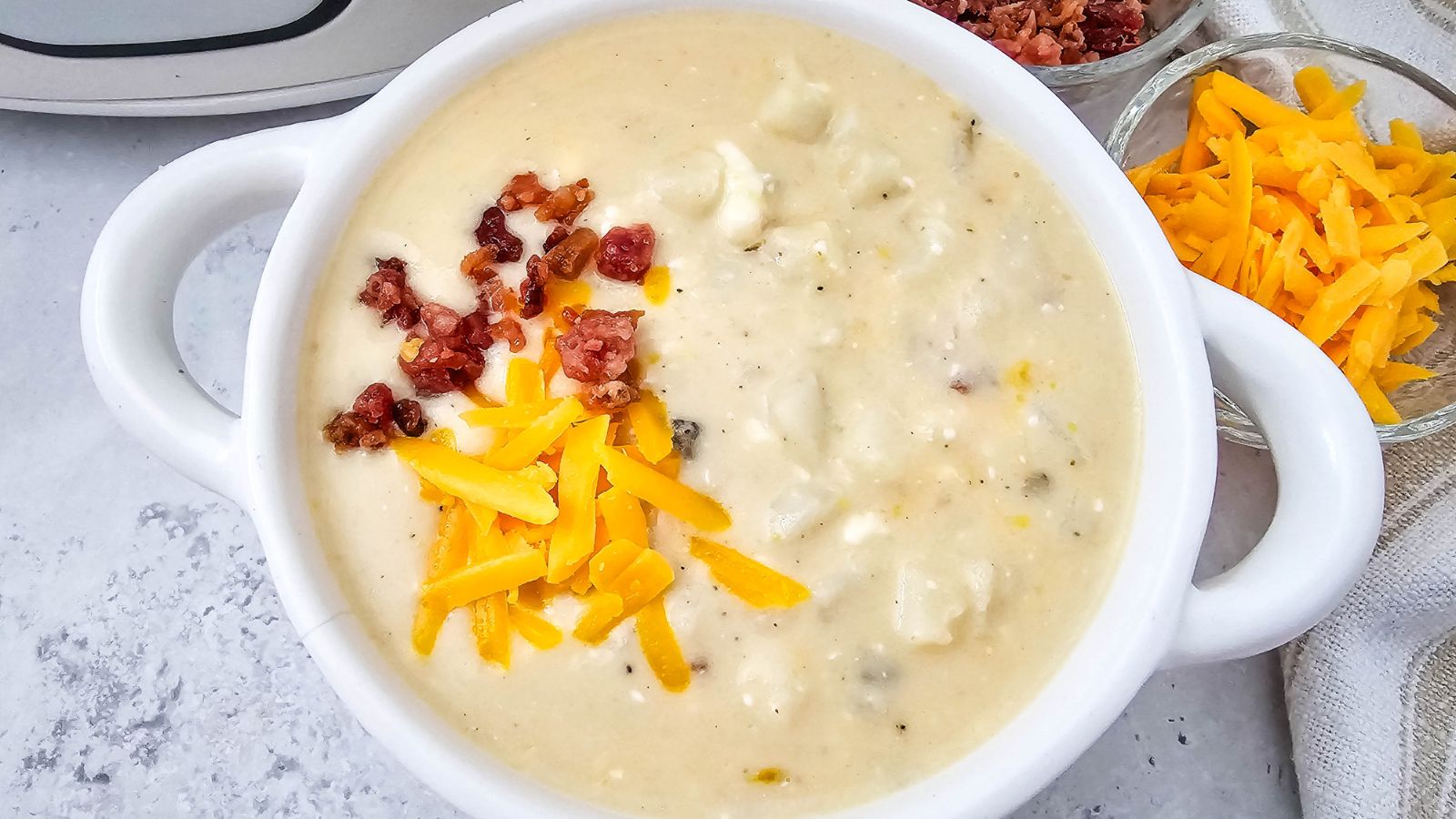 White bowl with loaded baked potato soup topped with cheese and bacon.