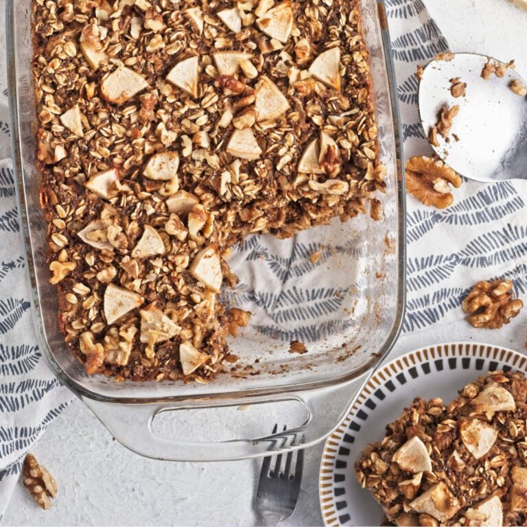 Baked apple oatmeal topped with apples in a glass baking dish and a slice out of it.